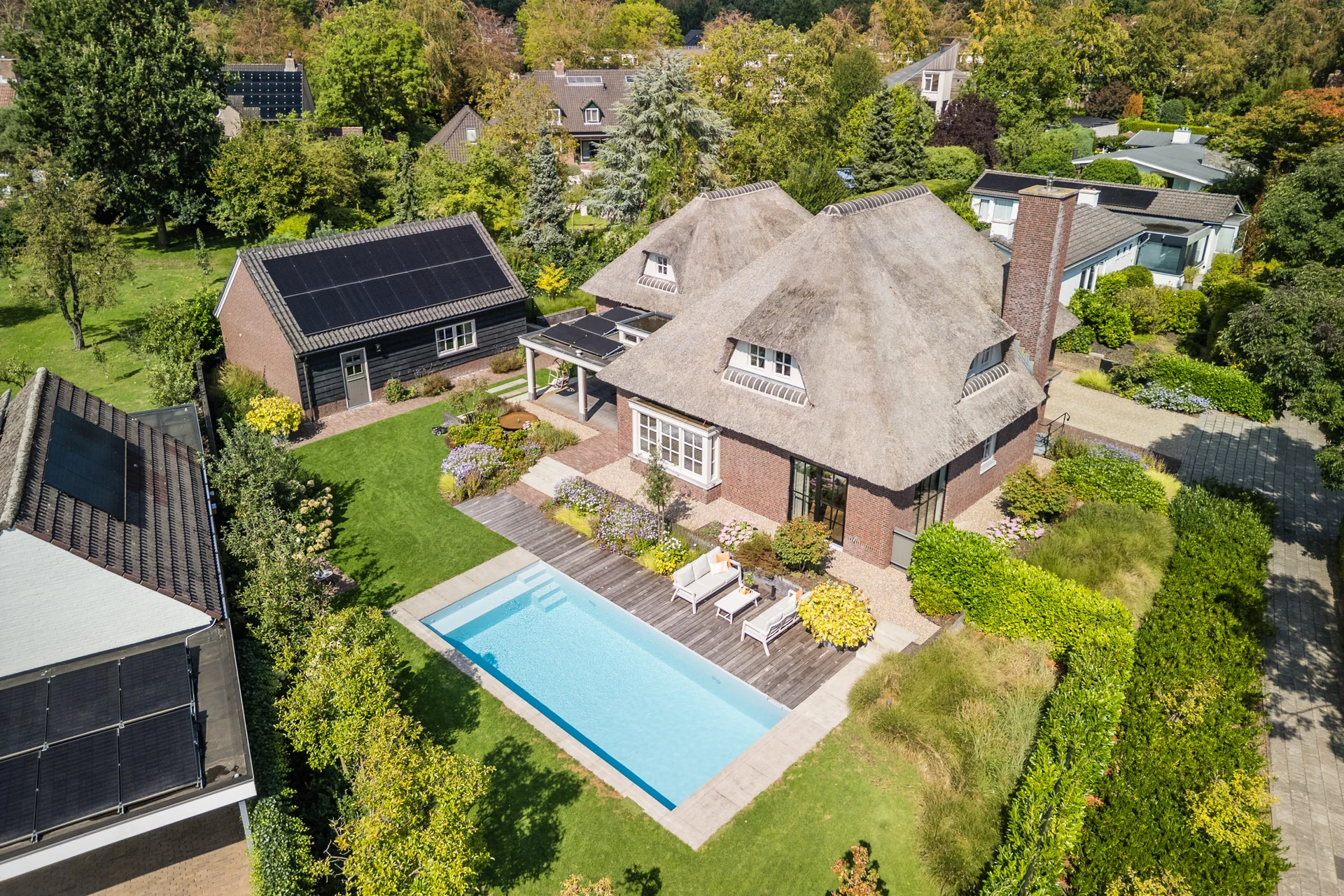 Drone photo of a detached home with a thatched roof, garden and pool
