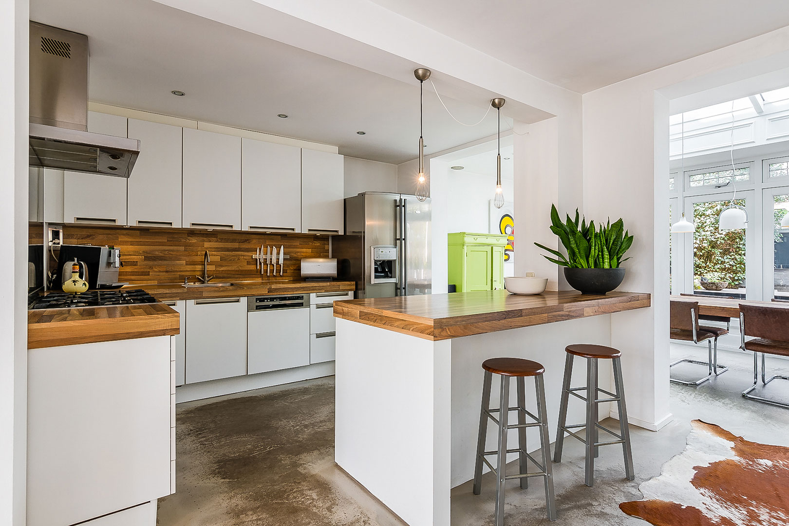 White open-plan kitchen with a wooden worktop and bar stools